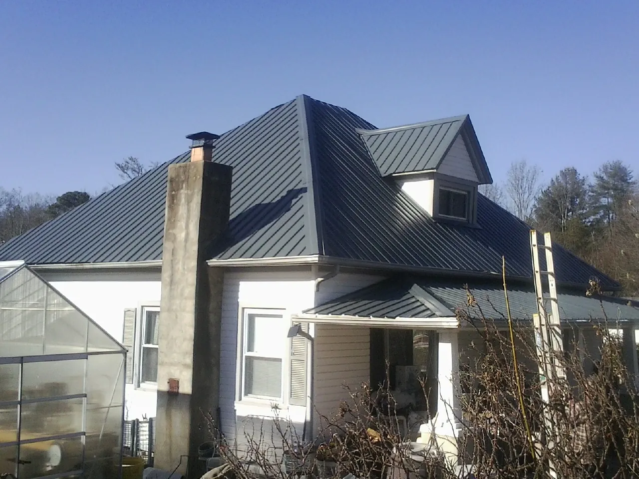 Dark blue standing seam metal roof on a white farmhouse with dormer — Slate & Tile Roof Repair by Roofing Brothers in Hematite