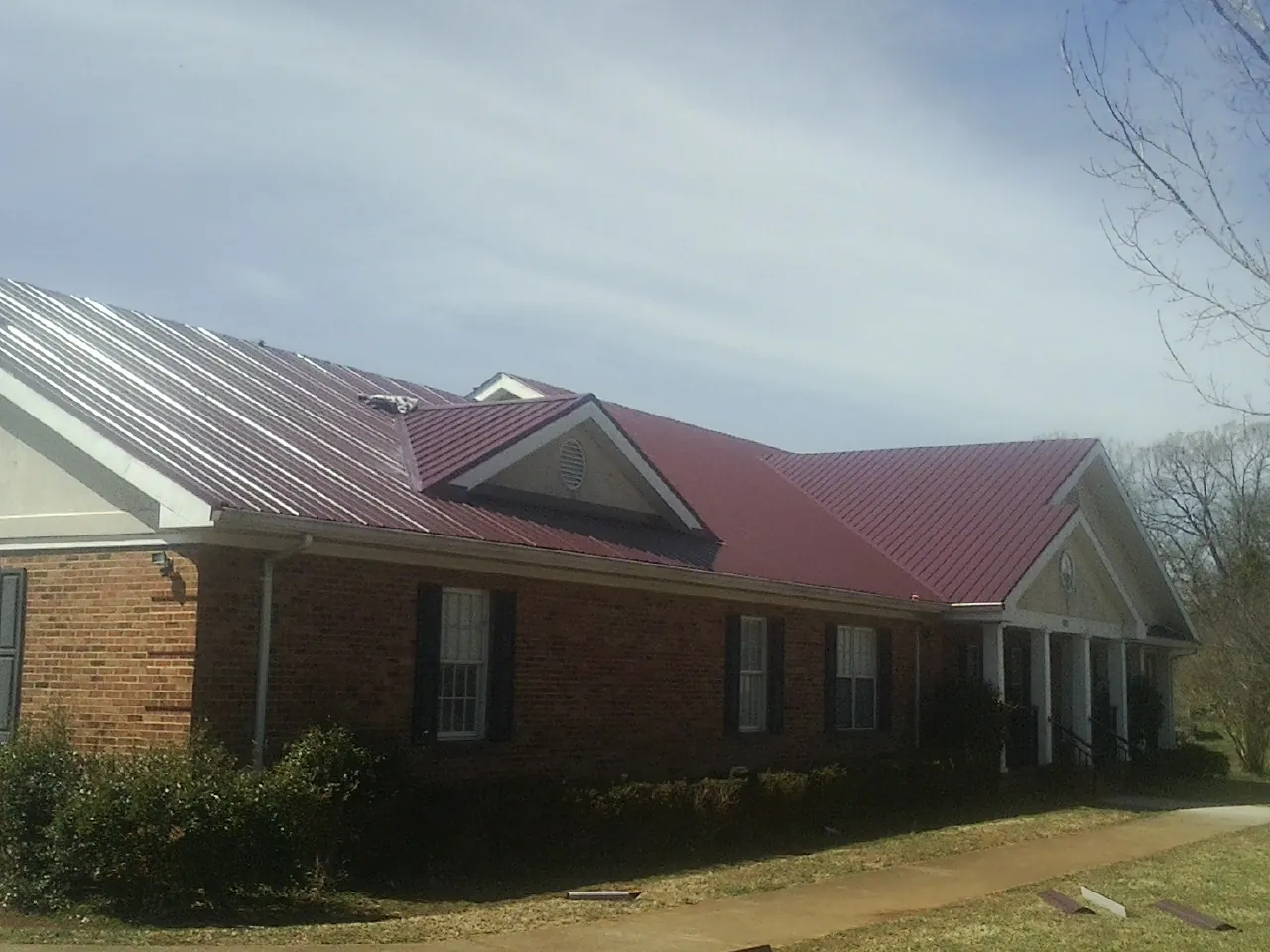 Red metal roof with gabled entries on a long brick building, from a Hail Damage Roof Repair job in Hematite
