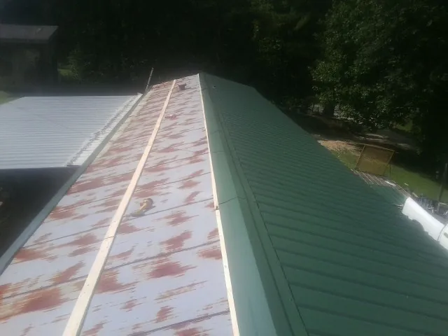 Old rusted panels beside newly installed green metal roofing — Wind Damage Roof Repair by Roofing Brothers in Hematite