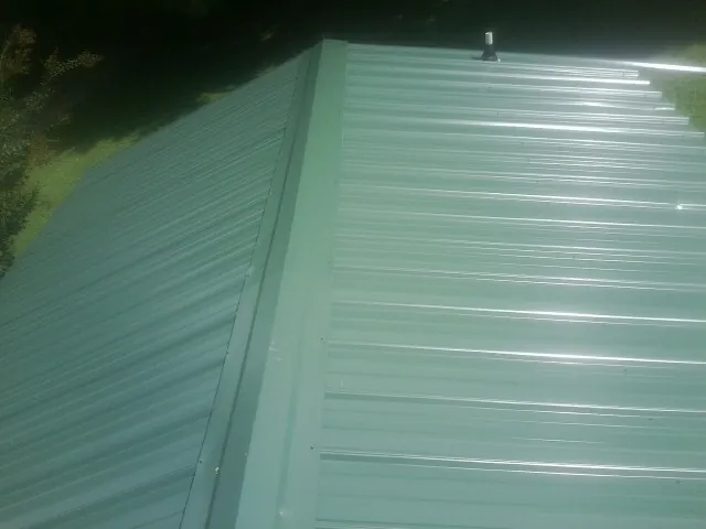 New green metal panels meeting at the ridge of a roof — Flat Roof Repair work by our crew in Hematite