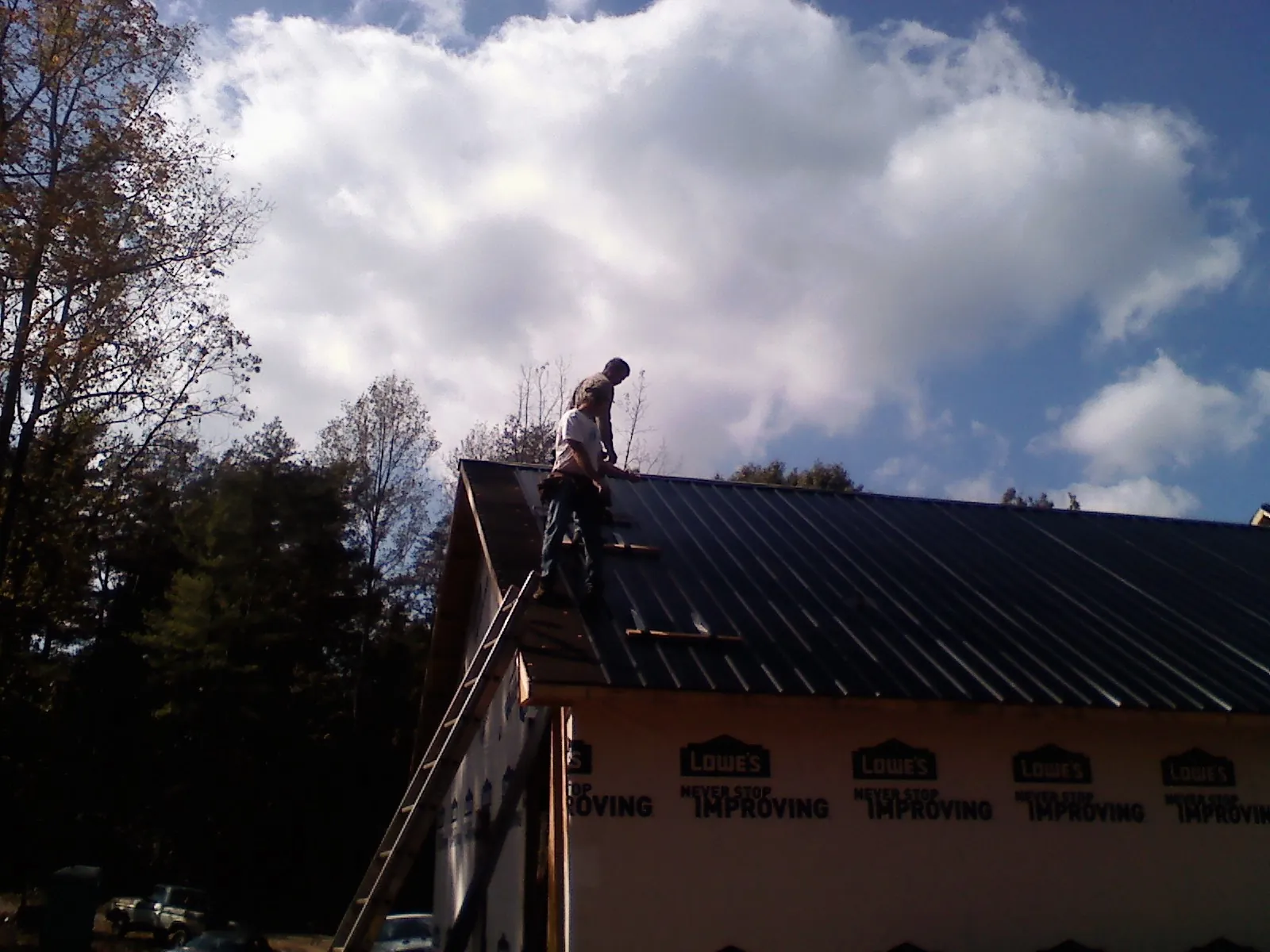 Roofer fastening dark metal panels high against a cloudy sky, from a Roof Inspection job in Hematite
