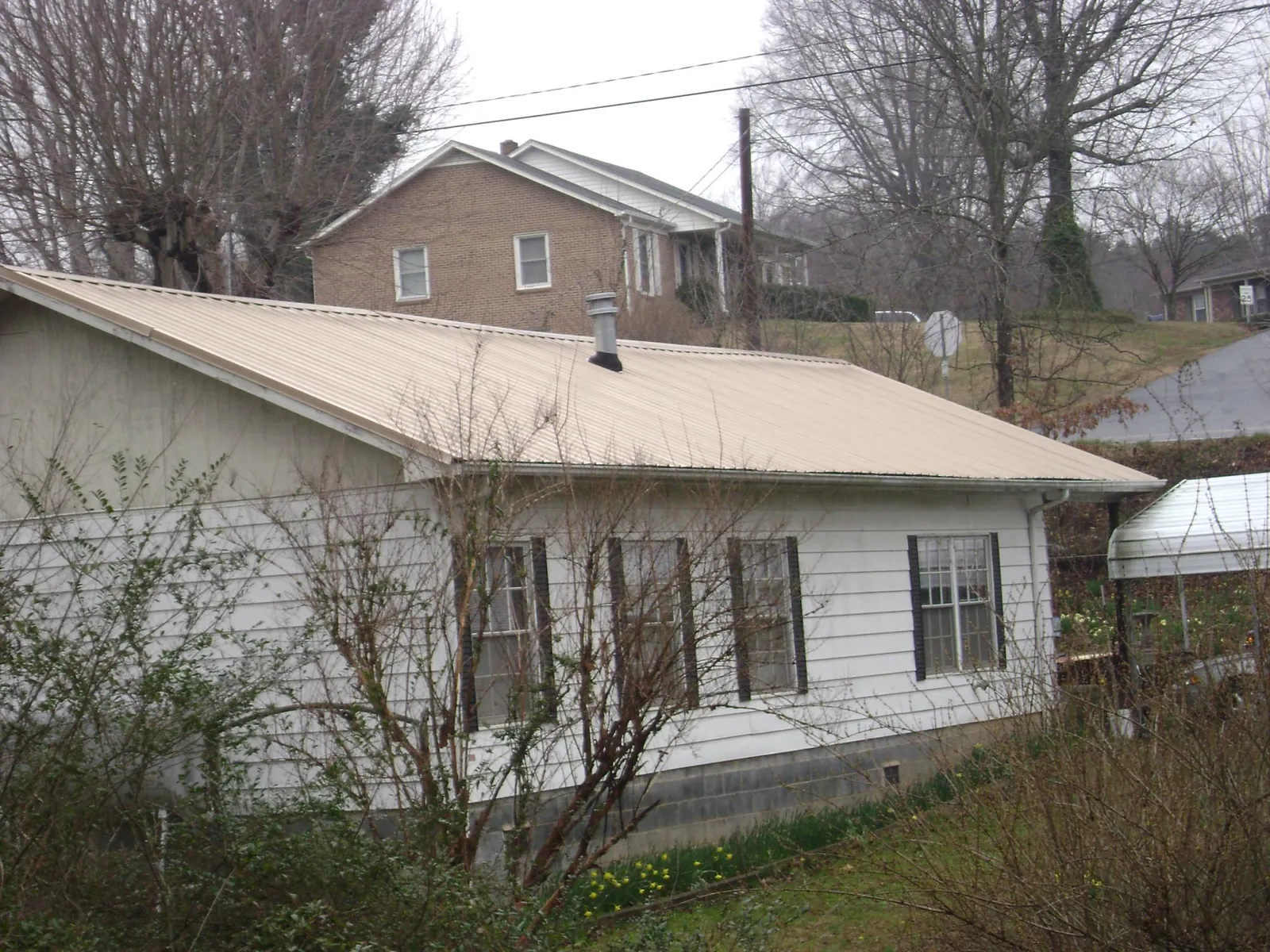 Tan metal roof on a white sided house set into a hillside — Commercial Roofing by Roofing Brothers in Hematite